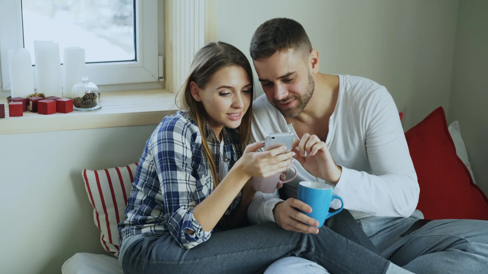 A couple sitting together in bed while checking a smartphone to research Nurx alternatives for PrEP and select the best online PrEP provider.