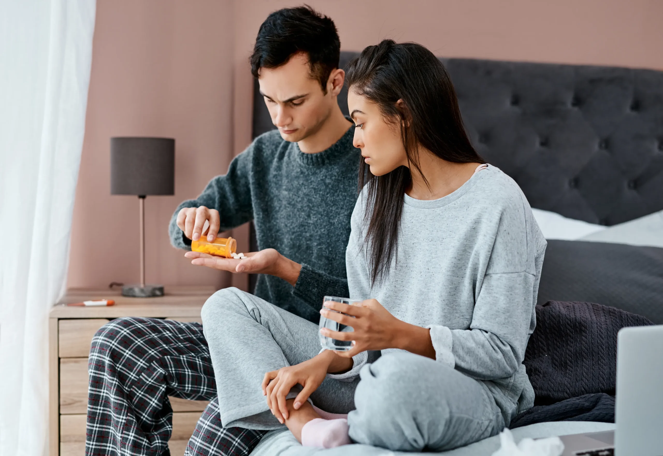 A couple sitting on a bed while a man pours pills from a prescription bottle, illustrating the daily routine of managing PrEP Medication.