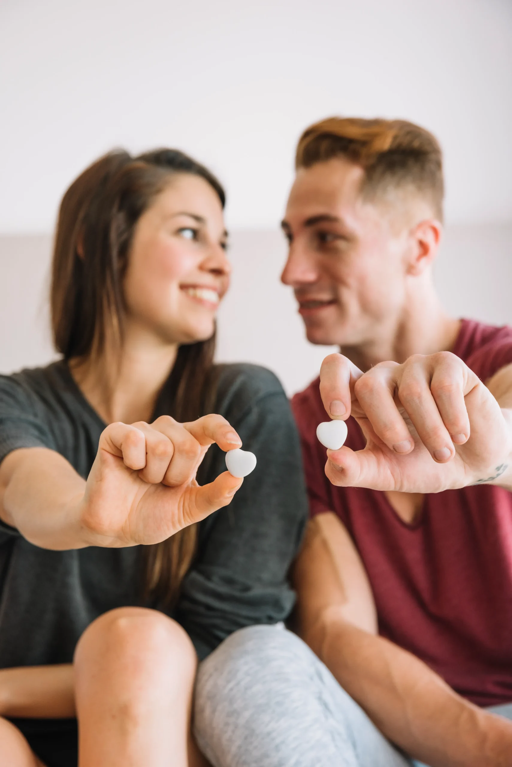 A close-up of a smiling couple holding heart-shaped pills, highlighting safe sexual health practices for individuals deciding who should take PrEP.