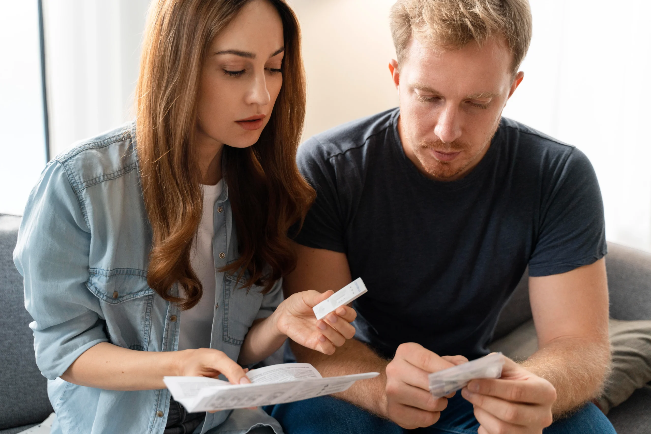 A young couple at home carefully reviewing a medical instruction packet and an rapid test kit, discussing how to get PrEP online through confidential PrEP access channels.