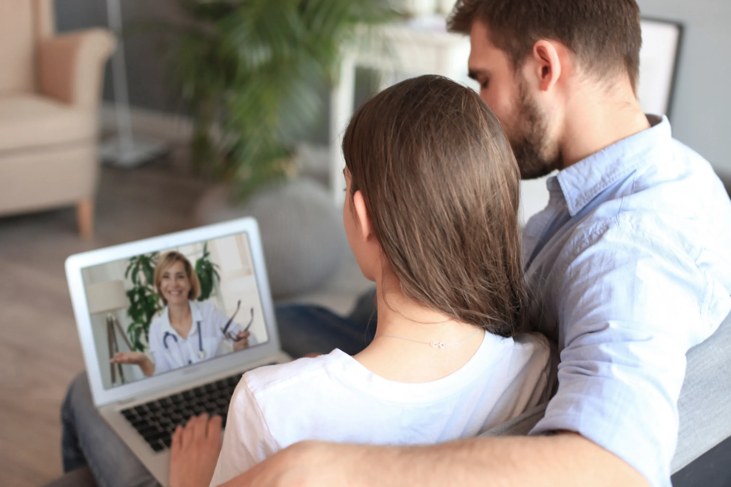 A couple sitting on a couch using a laptop to consult a telehealth doctor for online PrEP.