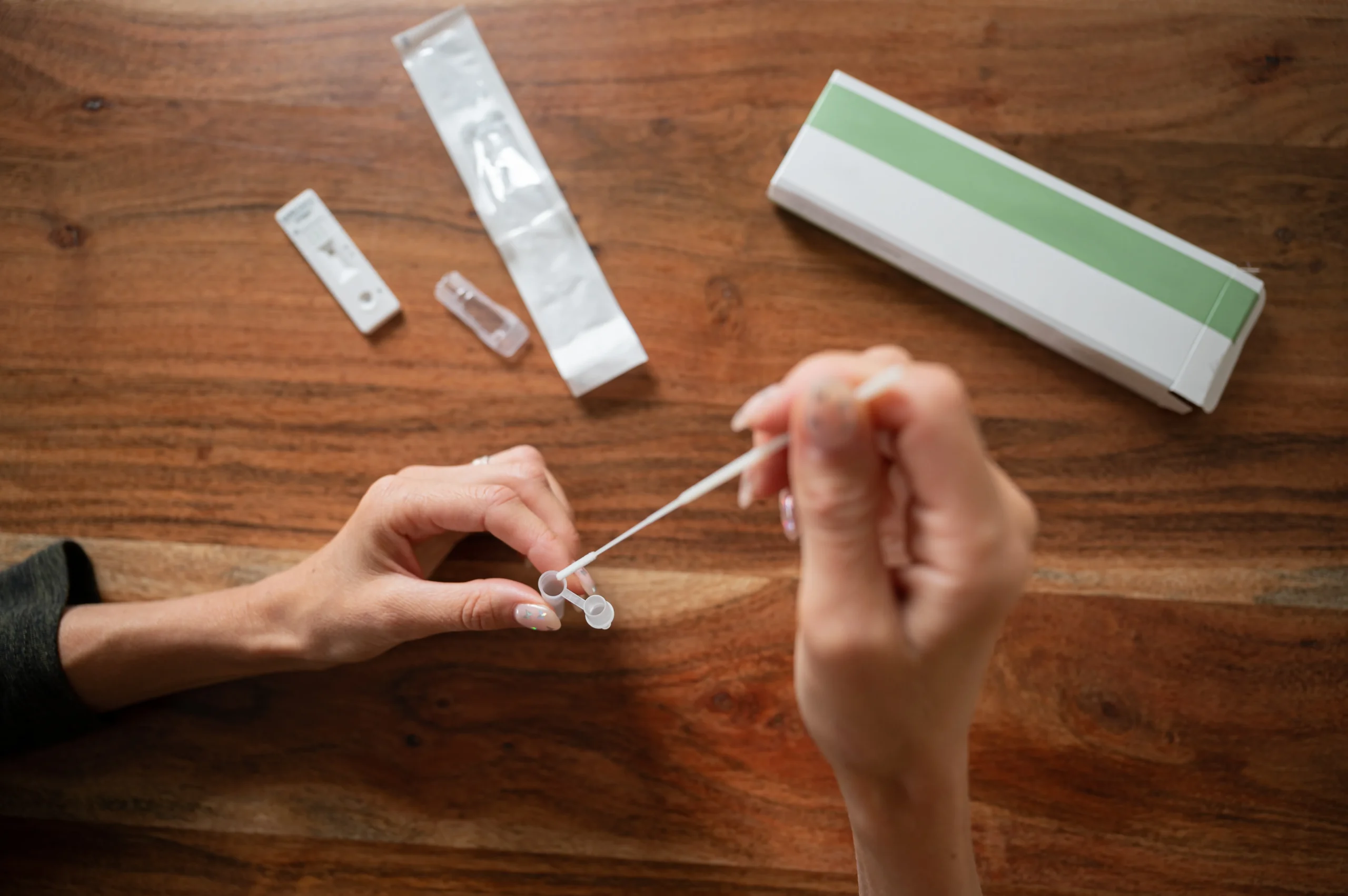 Close-up of hands preparing a sample using an at home STI test component on a wooden table.