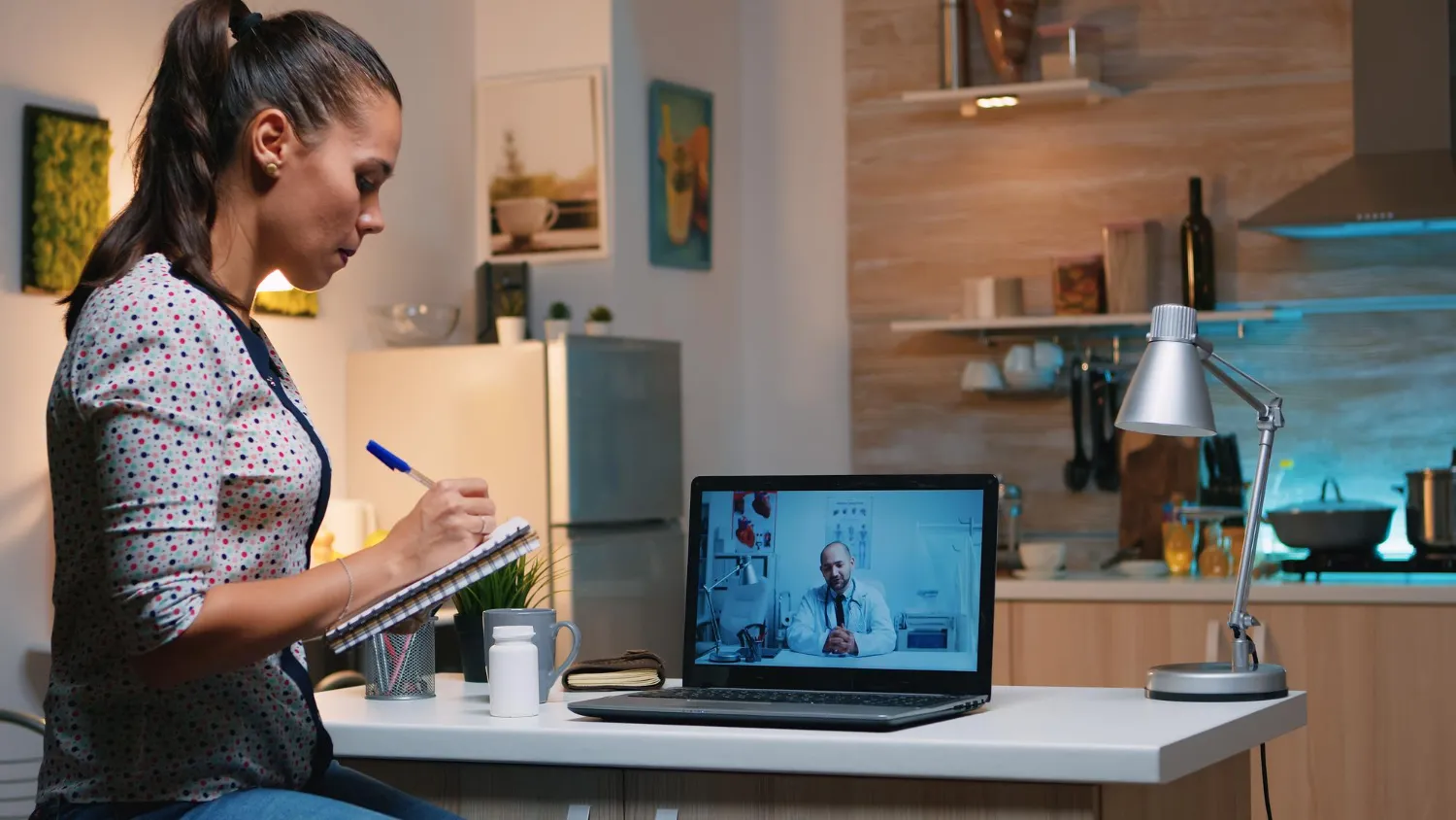 A woman taking notes during a PrEP telehealth video consultation with a virtual doctor on her laptop.