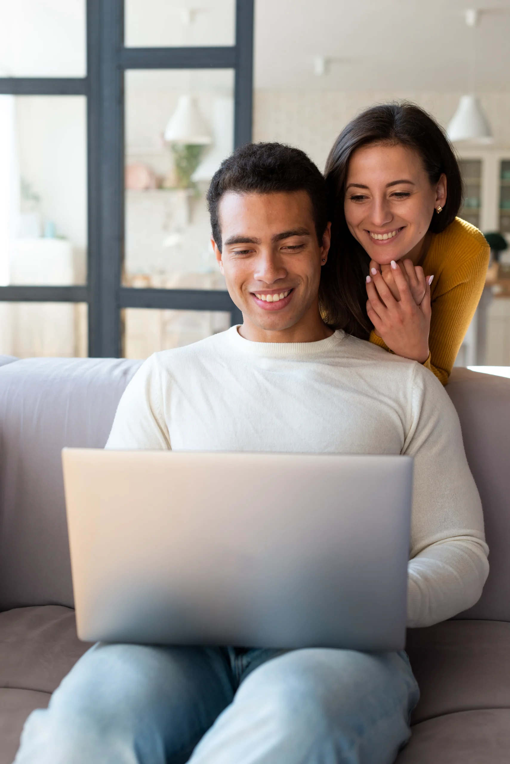 A happy couple sitting on a sofa looking at a laptop to access online PrEP services for HIV prevention.
