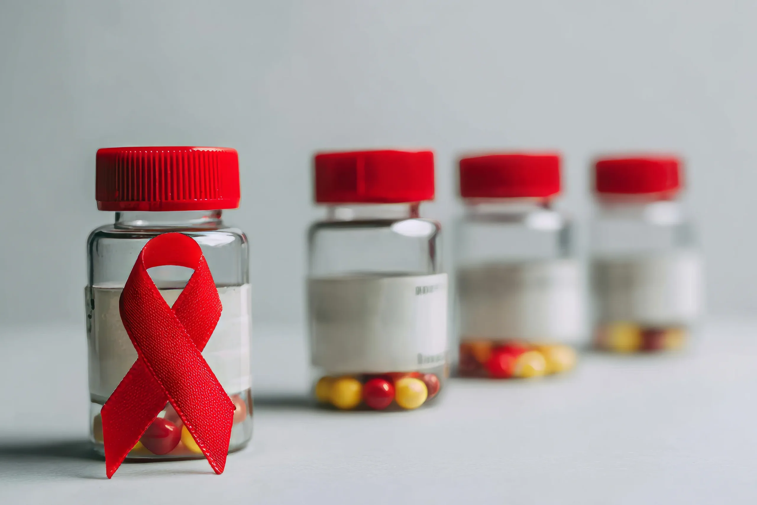 Clear prescription pill bottles with a red awareness ribbon representing daily HIV prevention treatment options.