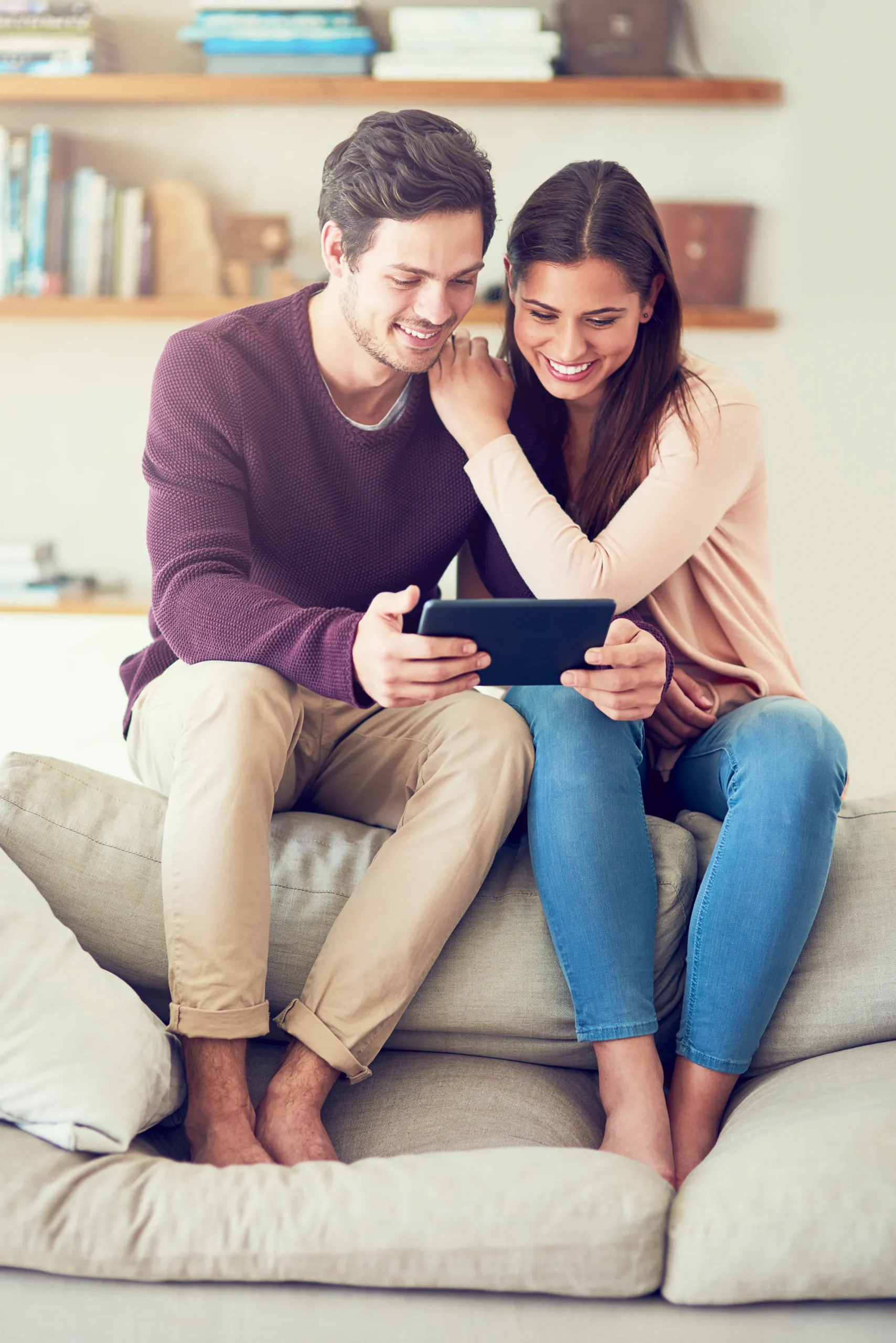 A happy couple sitting on a couch browsing a tablet screen together to look for PrEP online options.
